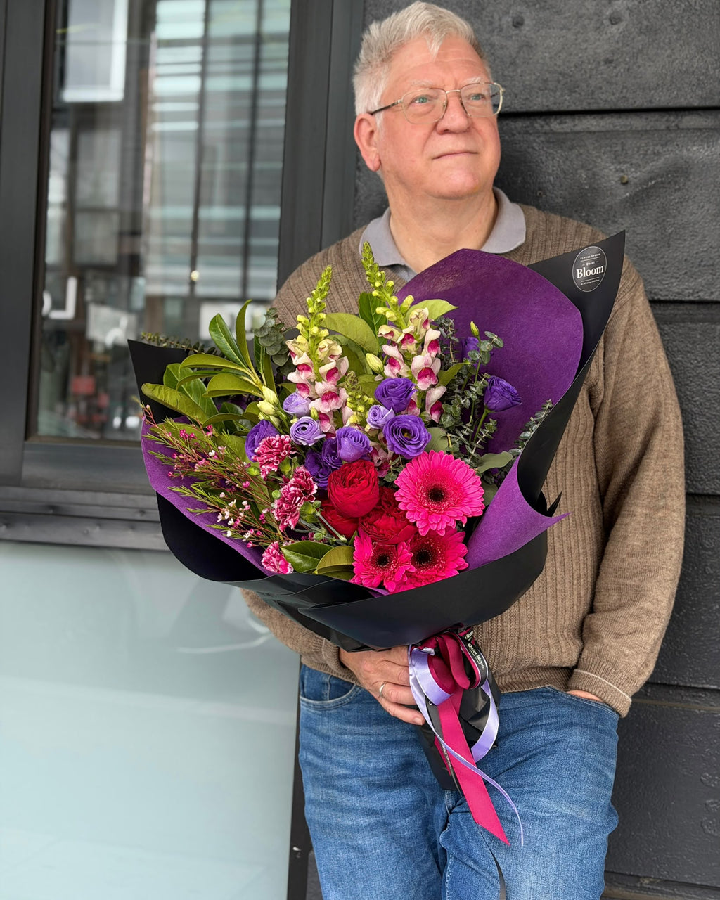 Purple and pink flower bouquet featuring lisianthus, pink gerberas, red roses and snapdragons in purple and black wrapping by Quiet Bloom Richmond.