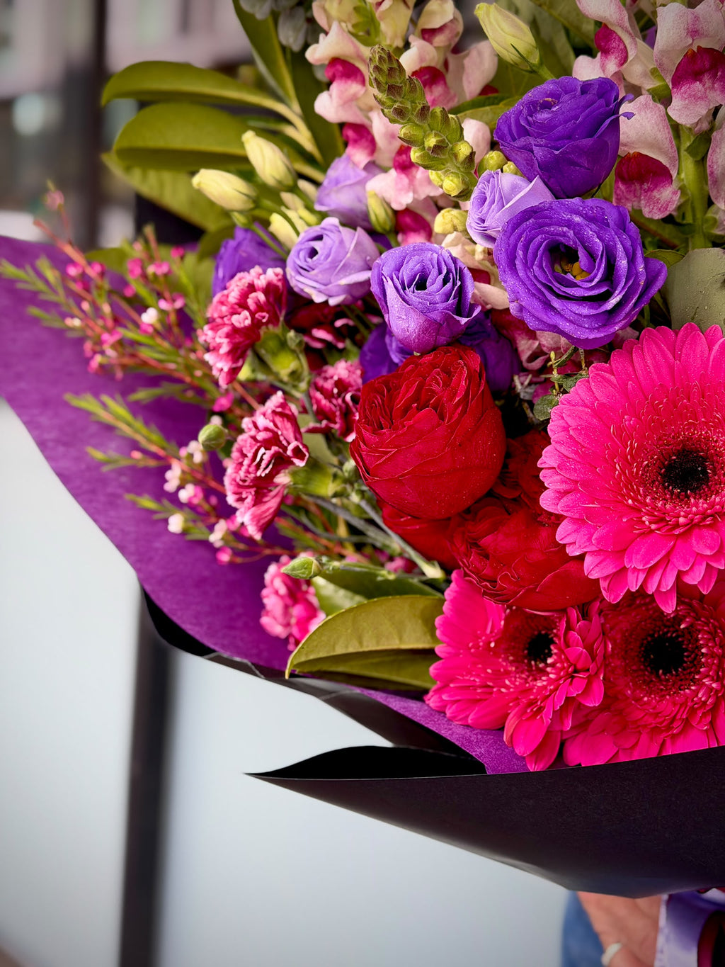 Side view of Violet Passion bouquet with purple lisianthus, red roses, bright pink gerberas and pink snapdragons, wrapped in purple and black paper by Quiet Bloom Richmond.