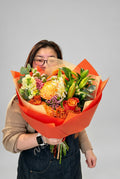 Large orange and yellow flower bouquet with orange roses, golden chrysanthemums, lily buds and seasonal greenery in orange wrapping, handcrafted by Quiet Bloom Richmond.